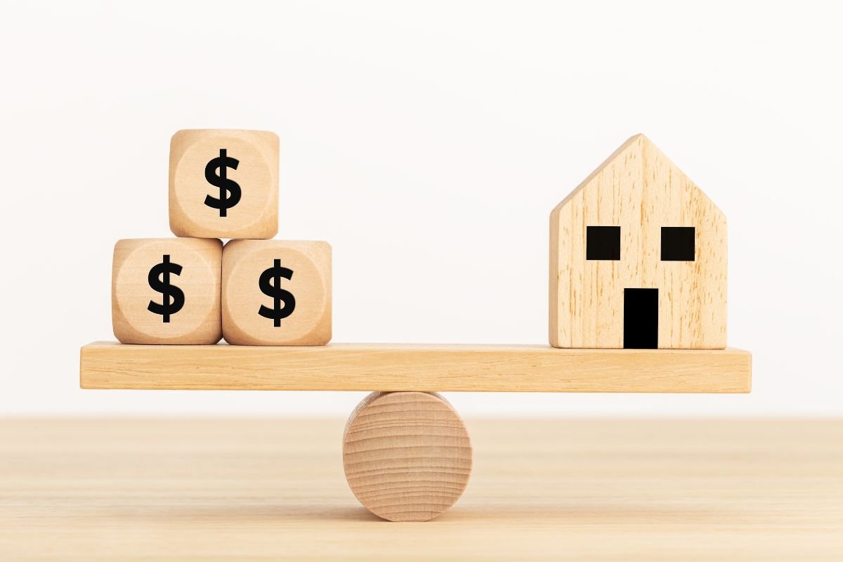 Fakockákból készült mérleg, egyik oldalán egy házat ábrázoló fakocka, a másik oldalon dollárjelű fakockák, az ingatlan értékbecslés szimbolizálására.